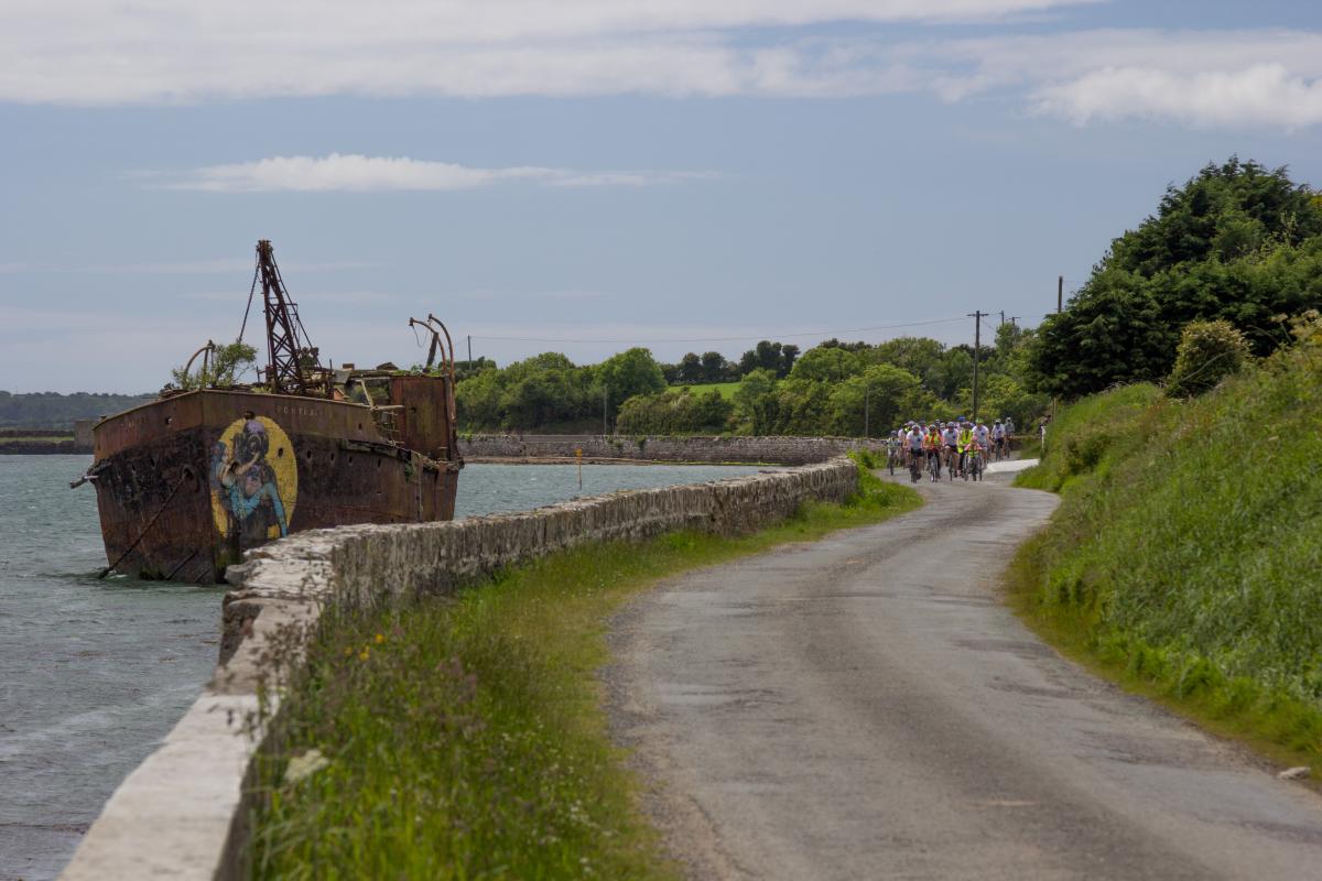 group of cyclists on coastal road near ship wreck